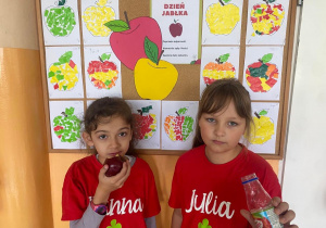 dziewczynki w czerwonych koszulkach na tle prac plastycznych nt. jabłek